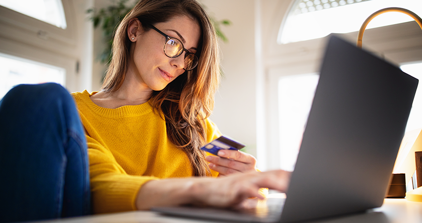 Cropped photo of a person in front of a laptop holding a credit card whilst typing on the keyboard